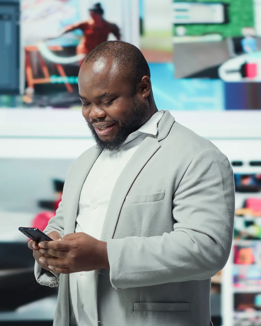 A customer in a grey blazer smiles at his phone in front of a wall of bright screens